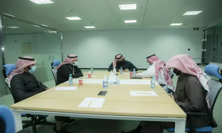 يجتمع خمسة أشخاص من الفريق الطبي، مرتدين الغترة أو الشماغ والعقال والبشت السعودي، حيث يوجد عدد كبير تتوزع عليها الأوراق. ويقام هذا اللقاء المهني في مكتب حديث مضاء بشكل جيد داخل مدينة جامعة القصيم الطبية، حيث يناقش المجتمعون الشاملون فيما يتعلق بالعمل الخاصة بالعمل الطبي ضمن بيئة تضامن هوية الجامعة الوطنية.