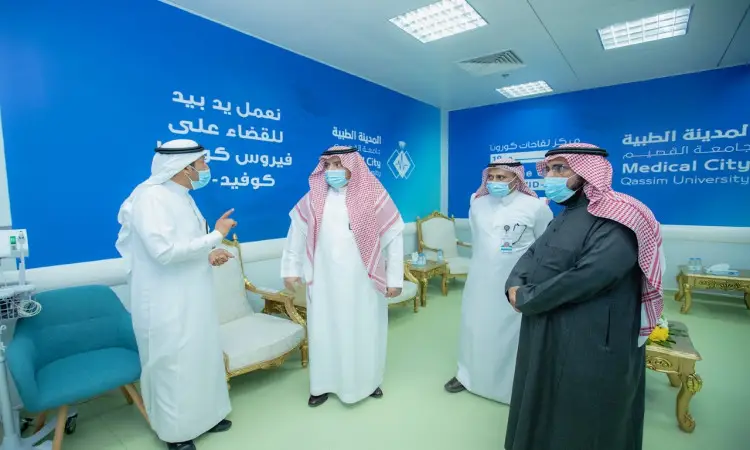 يتبادل أربعة رجال الغترة أو الشماغ السعودي مع العقال والبشت السعودي الأحاديث داخل مستشفى الجامعة المضيء في جامعة القصيم، مرتدين الكمامات الطبية. تأخذ على الجدران لافتات زرقاء باللغة العربية الشاملة بالتوعية حول فيروس كورونا والإرشادات الارشادية الخاصة بـ COVID-19.