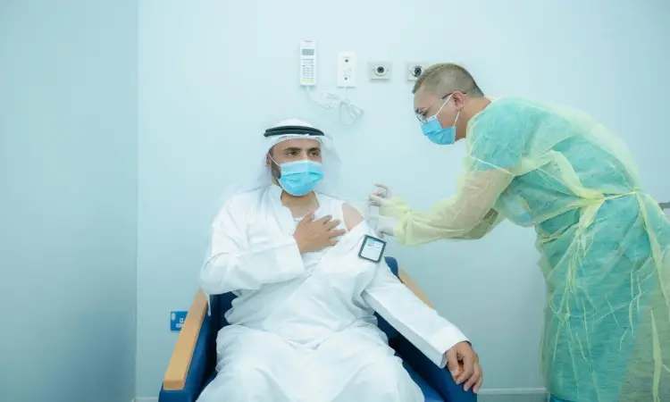 يقوم أحد العاملين في الرعاية الصحية، مرتدياً معدات وقاية شخصية، بإعطاء باحث في مركز التطعيم ضد فيروس كورونا لمستشفى الجامعة في القصيم لرجل يجلس مرتدياً شماغاً أو غترة وعقالاً وبشتاً سعودياً بالإضافة إلى كمامة طبية.