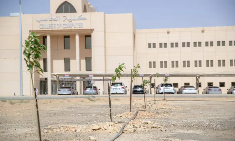 Rows of small works, planted as part of the "Green Cover in Qassim" campaign, are seen organized in the moist soil in front of the white-colored building of the College of Computer Science in Qassim. A number of cars are lined up in the background. The presence of young Saudis wearing the Ghutra or Shemagh and Eqbal, along with Saudi Bisht shirts, emphasizes the accuracy and authenticity of the national look within the corridors of the university.