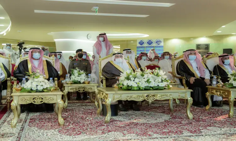 طقم جلوس من الرجال مرتدين الغترة أو الشماغ والعقال، بالإضافة إلى البشت السعودي، على فخمة تتزين بترتيبات زهور؛ وذلك أثناء وجودهم في المنزل في جامعة القصيم. وأخيراً في الخلفية عدد من الأفراد وأفراد الأمن الذين يلمسون سير العمل.