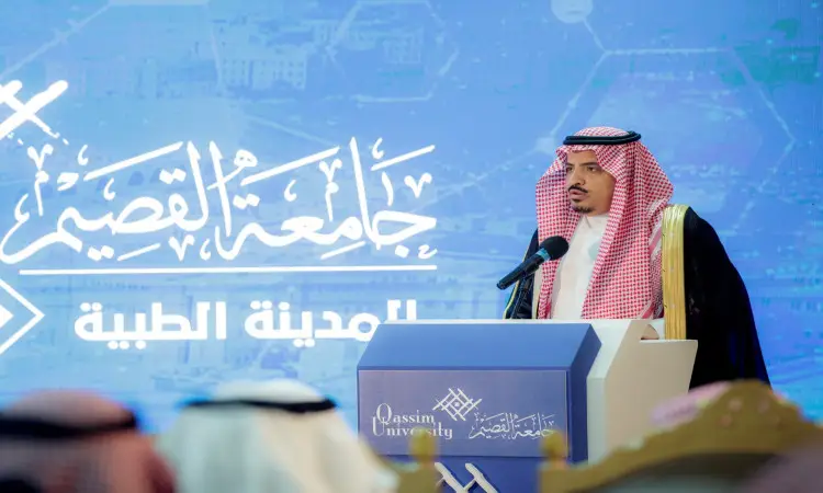رجل يحتال مرتدياً البشت السعودي مع الشماغ والعقول أمام المشاهير خلال جلسة الفعاليات في المدينة الطبية في القصيم. يعتقد خلفه أنه يحمل اسم الجامعة باللغتين العربية والإنجليزية يغلب عليه اللون الأزرق، بينما يبدو في المجموعة من الحضور يتابعون الحدث.