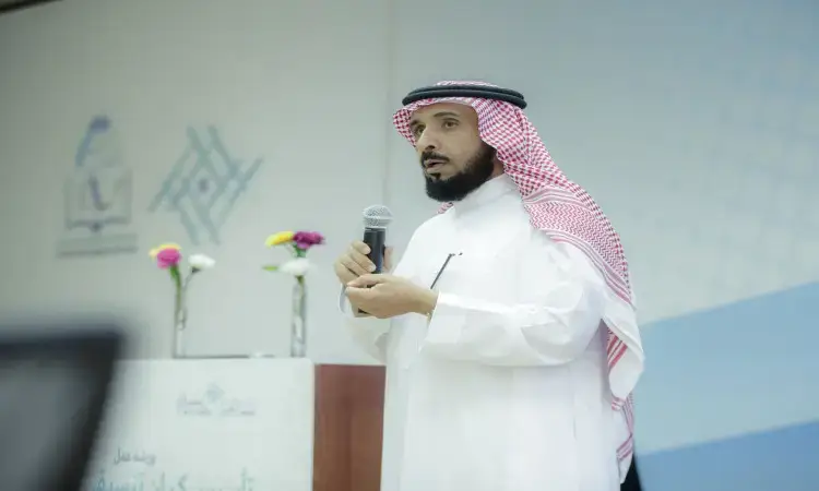 رجل خاطرة سعودية وبشتاً سعودياً، الاتصال خلف منصة الزينة بالزهور ويتحدث عبر الميكروفون في المدرسة، بينما يتتبع بصماته ونصوصه العربية ويتفاعل مع القصيم وشركاء التنمية المحلية.