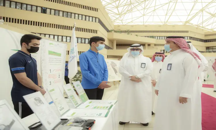 التجمع من الرجال داخل الوحدة القاعات، حيث يجتمع الغتة أو الشماغ مع العقال والبشت السعودي، في حين يظهر أني بزيّهم الرسمي. اجتمع الجميع حول طاولة عرض تتضمن ملصقات توعوية حول مبدعي مضخة، وقد حرصوا على ارتداء الكمامات الطبية بشكل تماشياً مع تدابير الاحترازية. يأتي ذلك ضمن فعاليات معرض توعوي أُقيم في جامعة القصيم.