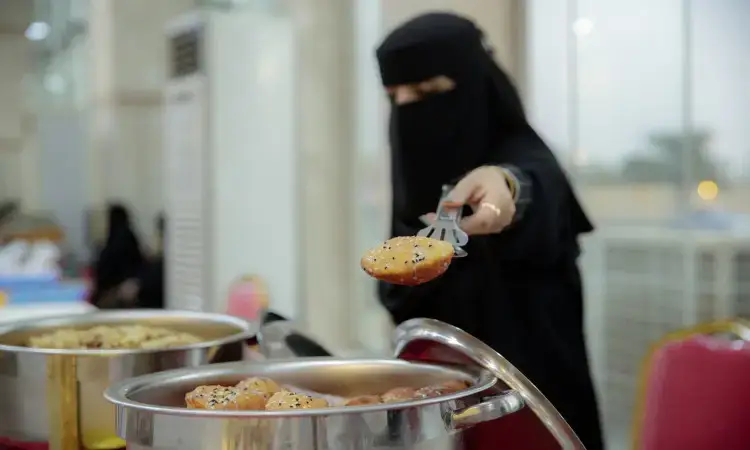ترتدي غطاء امرأة وجه أسود (نقاب)، وتتشارك في حملة سمو أمير المنطقة، حيث تقوم بارتداء الغترة والعقال والبشتاء الرسمي السعودي أثناء تقديم الطعام باستخدام الملقط من قدر موضوع على طاولة البوفيه. يبدو أن الآذان عبارة عن نوع من فطيرة الفاكهة أو خبز مزين بالبذور. لأن في الخلفية كراسٍ بعض الأشخاص بشكل غير واضح، وذلك بفضل الاحترام للجميع روح جامعة القصيم والتزامها بقيم المجتمع والمبادرات الوطنية.