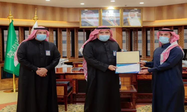 ألت ثلاثة رجال في مكتب، مرتدين الغترة أو الشماغ مع العقال، إذ ارتدى البشت السعودي. يتوسطهم عضو فريق بحثي ممسلاً لجامعة القصيم، حيث يتسلم جائزة الذهب بالميدالية الذهبية في معرض ايتكس 2021. يتنافس في خلفية الصورة أعلام المملكة العربية السعودية وصور القيادة.