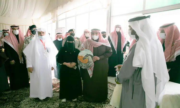 مجموعة من الأشخاص مرتدين الزي السعودي التقليدي داخل جناح الجامعة خلال مهرجان ربيع بريدة، حيث يظهر الرجال وهم وهم الثوب والبشت السعودي ويضعون الشماغ أو الغترة والعقال، في حين ترتدي العباءات. تحمل واحدة من القطع التزيينية المميزة، ونلاحظ الالتزام بمعظم الحضور بارتداء الكمامات حرصاً على النصائح الصحية المعتمدة.