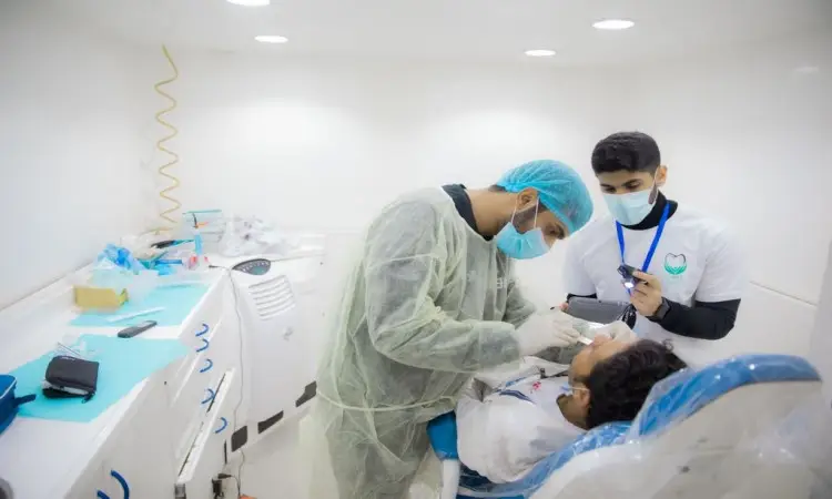 يقوم طبيب أسنان مرتدياً البشت السعودي والغترة بفحص أسنان الطفل في عيادة مركز مركز لطب الأسنان، بينما الاتصال إلى جانبه مساعد من قوافل طب الأسنان في القصيم مرتداً العقال والغترة السعودية ويسجل الملاحظات. وتبدو العيادة نظيفة ومضيئة بشكل جيد، مع ظهور الأجهزة الطبية في الجدول.