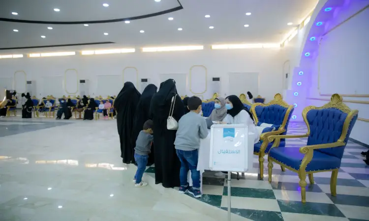 مجموعة فلوريدا من مرتديات العباءات السوداء، ويرافقهن عدد من الأطفال، عند مكتب المساعدات الإنسانية في قاعة مضيئة كراسٍ زرقاء في مركز قبة الجامعة في القصيم. في صفحة صغيرة من لوحة تحمل نصاً باللغة العربية للتعريف بمبادرة "قوافل طب الأسنان". كما تواجد بعض الرجال مرتدين الشماغ السعودي أو الغترة البيضاء مع العقال والبشت السعودي، بما في ذلك الطابع الرسمي والموروث الوطني الأصيل للمكان.