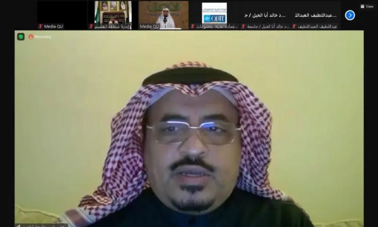 رجل يرتدي نظارة، ويضع شماعاًقالاً فوق شماغ سعودي تقليدي، كما يرتدي بشتاً رسمياً رسمياً، أمام الجميع خلال الاجتماع الافتراضي عبر منصة Zoom. وقد تناول برنامج الجامعة، بحضور عدد من قيادات الدائرة الحكومية الذين يظهرون صورهم في نافذة صغيرة أعلى الشاشة.