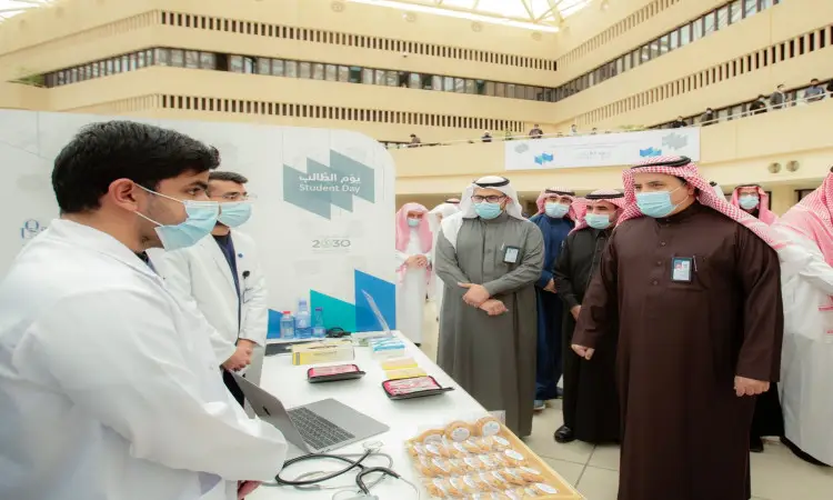 مجموعة من الناس، وترتدي معظمهم الكمامات الطبية بالإضافة إلى الغترة أو الشماغ والعقال، كما يتضح من مرتدين البشت السعودي، الاتصالون حول طاولة تحتوي على مستلزمات طبية وفي الفعالية وتحمل شعار "يوم الطالب". ويلاحظ حضور رئيس جامعة القصيم عدد من أعضاء الأندية الطلابية وهم يستمعون باهتمام إلى شرح يقدمه أحد المختصرين مرتدياً المعطف الأبيض.
