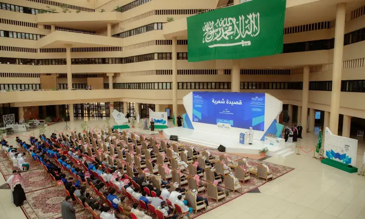 يقام مؤتمر أو ندوة في قاعة واسعة تكتظ بصفوف الحضور الجالسين، ويرتدي العديد منهم الغترة السعودية أو الشماغ السعودي مع العقال، وأقل عدد من المشاركين بالشت السعودي الرسمي. يعلو علم المنصة المملكة العربية السعودية الأخضر، حيث يتفضل معالي الكبير رئيس جامعة القصيم بإلقاء كلمته تحت لافتة زرقاء وبيضاء احتفاء بيوم الطالب.