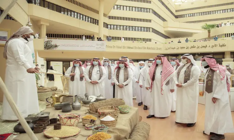 يجتمع مجموعة من الأشخاص تولى الزي السعودي الأصلي، بما في ذلك رئيس الجامعة الذي ارتدى الشماغ والعقال والبشت السعودي، لمتابعة معرض يوم تانكس في ردهة الداخلية الحديثة، والذي يشتمل على مأكولات وتحف تستعرض جانباً من تاريخ الدولة السعودية. كامل الحضور ملتزمون بارتداء الكمامات الطبية، بينما يقوم أحد المشاركين بإلقاء كلمة من خلف طاولة العرض.