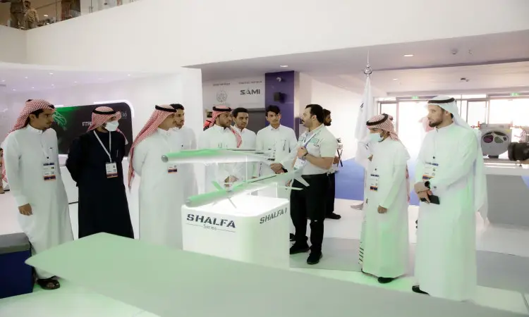 A group of men dressed in Saudi Arabia's Ghutrah, Shamaa, Aqal and Bisht around a model drone called Shalva at the Global Defense Exhibition in Riyadh, listening intently to Qassim University students as they introduce and explain this distinction.