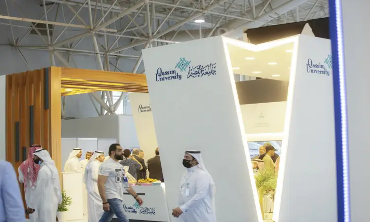 Visitors walk around Qassim University's modern pavilion at the Middle East Poultry Exhibition in Riyadh. It is characterized by flexible designs bearing the university's logo and texts in Arabic. A number of visitors and speakers are seen wearing the Saudi Shemagh or Saudi Ghutra with a headband, in addition to a Saudi video performance, in a scene that reflects the authenticity of the national identity and the university's distinguished academic mission.