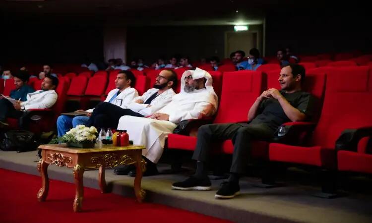 يحضرون، وغالبيتهم من الرجال الذين حضروا الغترة أو الشماغ والعقال، ويضع الفرق البشت السعودي، على اجتماع الحمراء في قاعة المسرح خلال فعالية نظمتها جامعة القصيم. وتتوسط القاعة طاولة مزينة بالزهور، لكن أمام الصفوف الأولى. طالبة بإضاءة كافية، مع وجود عدد أكبر من الحضورون في الخلفية.