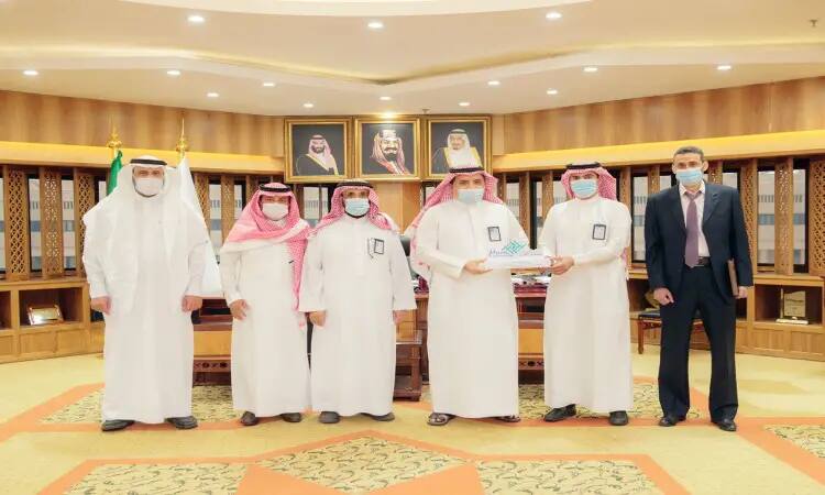 ستة رجال داخل النقابة، يرتدي منهم خمسة الزي السعودي الرسمي المشارك من غترة أو شماغ وعقال وبشت سعودي بالإضافة إلى الكمامات، بينما يظهر السادس مرتدياً بدلة رسمية. اجتمعوا بعد ذلك صورة تاريخية لتوقيع العمل بتحدي الجامعين في جامعة القصيم، حيث قاموا بإعداد اثنين منهم قالب الحلوى. يؤخذ في الخلفية وثلاثة صور رئيسات بارزة.