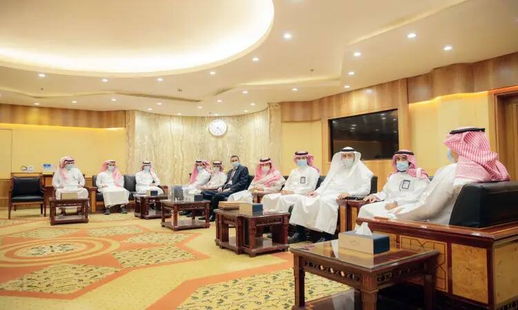 يجتمع مجموعة من الرجال، منهم رئيس الجامعة، في القاعة المتمثلة في فسيفساء ومضيئة ذات ديكور فاخر وساعة كبيرة ملحوظة. حضر البشت السعودي، والعقال، والشماج والغيترة السعودية التقليدية، بالإضافة إلى بعض الأشخاص الذين يرتدون الملابس الرسمية. يلتزم عدد من خطواتين بارتداء الكمامات حرصًا على السلامة أثناء المشاركة في لقاء تحدي مبدع الجامعي الذي ينظمه جامعة القصيم.