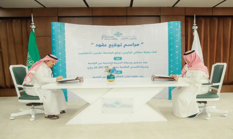 يرتدي رجلان الزي السعودي الرسمي المكون من غترة أو شماغوقال بالإضافة إلى بشت سعودي، إلى طاولة في قاعة السيدات داخل المدينة الجامعية. يقوم الرجلان بتوقيع مستندات تتعلق بالتشغيل والصيانة، بينما يحملان خلفهما لوحة كبيرة تحمل شعار جامعة القصيم ونصوصًا باللغة العربية.