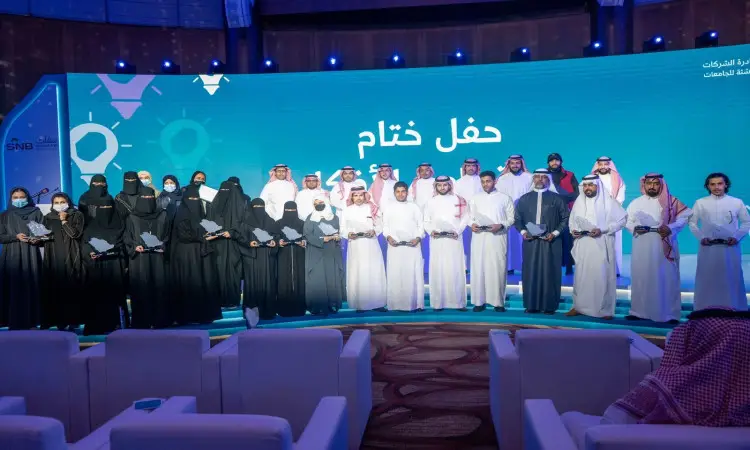 تجتمع مجموعة من الرجال بملابسهم التقليدية على خشبة المسرح في تيساس خلال تحدي باص الأفكار في جامعة القصيم. ارتدى الرجال شماغاً سعودياً وقالاً وبشتاً سعودياً، بينما يحضر بعض النساء بالنقاب وأقنعة الوجه. حضر المشاركون المؤتمرون لأفكارهم الإبداعية، وخلفهم شاشة زرقاء كبيرة تم عرض نصوصاً باللغة العربية، فيما يتابع حضور هؤلاء الحضور من مقاعدهم بإعجاب وتقدير.