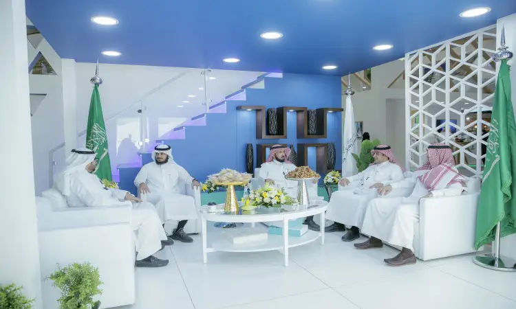 يجلس خمسة رجال تحت الغترة السعودية أو الشماغ والعقال، ويضع الشركاء البشت السعودي، حول طاولة خارجية فاخرة مجموعة من المأكولات المخصصة، وذلك في قاعة مضاءة بشكل جيد وزينة بإعلام المملكة وزهور جميلة في جناح جامعة القصيم خلال المؤتمر والمعرض الدولي للتعليم.