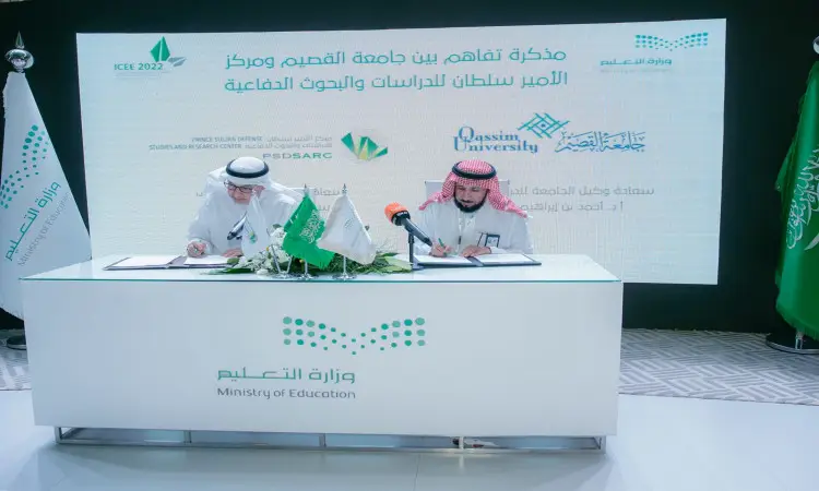 يجلس رجلان وينظمان الغترة والعقال والبشت السعودي حول طاولة، ويوقعتان اتفاقيات التعاون خلال المجتمع. يقفان خلفهما شعارات جامعة القصيم ووزارة التعليم السعودية، وبرز الأعلام السعوديين وأعلام الجامعة إلى جانب الملصقات التعريفية في المؤتمر الدولي للتعليم.