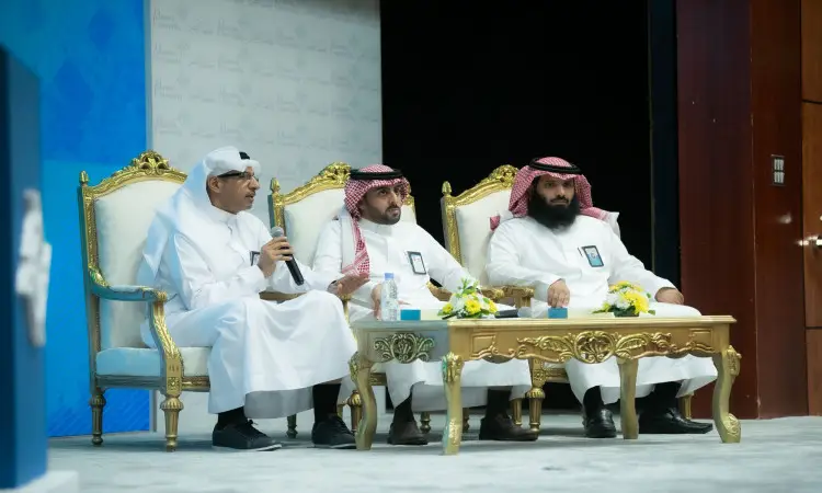 يجلس ثلاثة رجال ينتظرون الغترة أو الشماغ والعقال والبشتاء السعودي على كراسٍ فاخرة خلف طاولة مزينة بالزهور، يشاركون في جلسة نقاشية مميزة ضمن فعاليات إحدى اللوحات في القصيم حول موضوع التحول إلى الفصول الثلاثة. ويمسك أحدهم بالميكروفون ملاحظاً بكلمته للحضور.