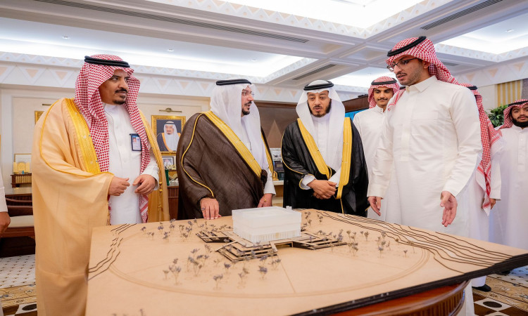 الاتصال مجموعة من الرجال مرتدين الغترة والشماع والعقال والبشت السعودي، جامعة طلاب الجامعة، حول مجسم معماري كبير يناقشون مشاريع المشاريع في قاعة فخمة تزيّنها صور مؤطرة و لهندسة راقية.