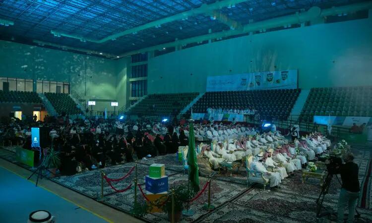 A great experience inside one of the halls of Qassim University, where a large number of men wearing the Ghutra or Shemagh and Egal in addition to the Saudi Bisht, followed by women in black abayas. The stands were filled with attendees under blue lighting, while the hall was decorated with flags and banners celebrating the distinguished students and the summer club.