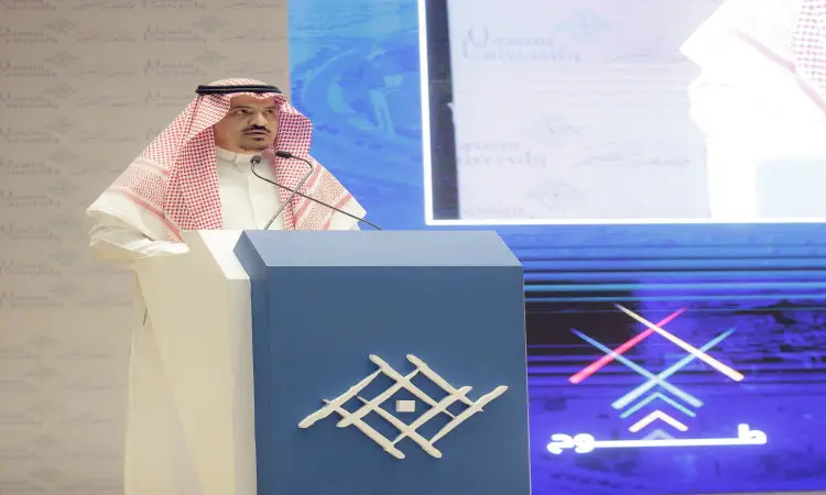 رئيس الجامعة، مرتداً الغترة والعقال والبشتت السعودي الرسمي، الجرس الكبير على المنصة التي تحمل شعار جامعة القصيم، متشوقاً كلمته للطلبة ويطلبون خلال برنامج طموح. للحفاظ على صورته وشعارات الجامعة بوضوح على الشاشة الكبيرة خلفه، في شهادة الاعتزاز بالهوية الوطنية الالتزام بالقيم الأكاديمية لجامعة القصيم.