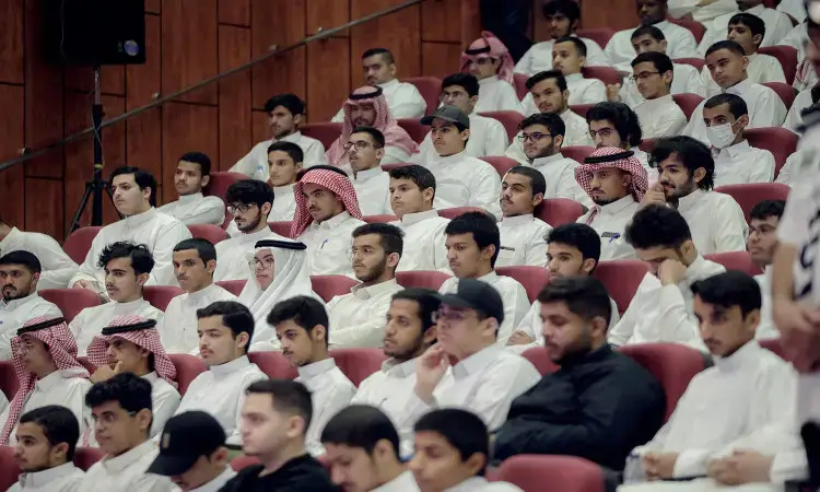 ليقوموا بجمع عدد كبير من الرجال، من بينهم الطلاب ويطالبون بتنظيم ترتيبات على الأقل داخل القاعة أثناء فعاليات البرنامج المطلوب في القصيم. ويظهر الحضور وهم الزي التقليدي السعودي كالغترة السعودية أو الشماغ السعودي مع العقال والبشت السعودي، بالإضافة إلى بعض الحضور بملابس غير عادية. ويبرز خلفية الصورة جداراً مزخرفاً بأبواب الثقة الفنان الرسمي للفعالية.