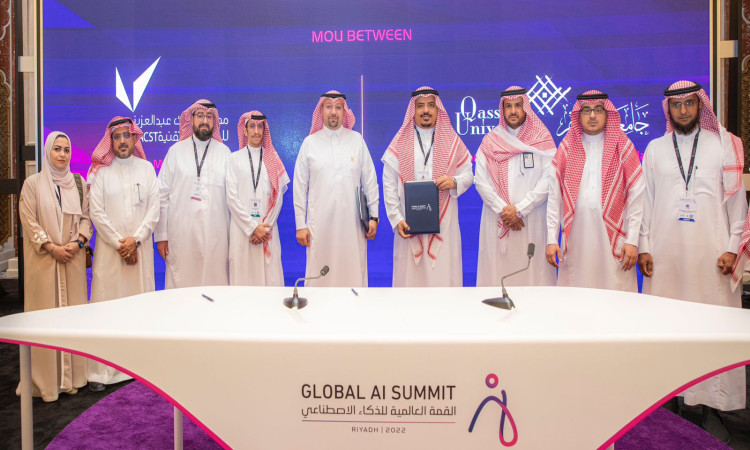 مجموعة الاتصال من الرجال الحاضرين الغترة أو الشماغ والعقال والبشت السعودي، بالإضافة إلى سيدة، على المسرح الخشبي خلال فعاليات القمة العالمية للذكاء الاصطناعي في الرياض. ونتيجة لشاشة الخلفية تحمل شعارات مدينة الملك عبدالعزيز للعلوم والتقنية. كما تتصدر طاولة الشطرنج تحمل شعار القمة في الفرق، بما في ذلك يضفي طابعًا وهنولوجيًا على الأحداث التي تشارك فيها جامعة القصيم.