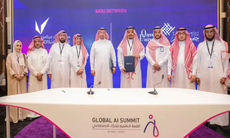 مجموعة الاتصال من الرجال الحاضرين الغترة أو الشماغ والعقال والبشت السعودي، بالإضافة إلى سيدة، على المسرح الخشبي خلال فعاليات القمة العالمية للذكاء الاصطناعي في الرياض. ونتيجة لشاشة الخلفية تحمل شعارات مدينة الملك عبدالعزيز للعلوم والتقنية. كما تتصدر طاولة الشطرنج تحمل شعار القمة في الفرق، بما في ذلك يضفي طابعًا وهنولوجيًا على الأحداث التي تشارك فيها جامعة القصيم.