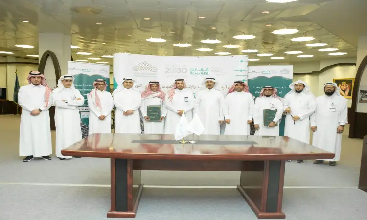 مجموعة ألت من الرجال الزي السعودي الرسمي، متوشحين الغترة أو الشماغ والعقال والبشت السعودي، مصطفين في صف واحدة داخل الالفات، أزرار خشبية للأطفال وأمامهم طاولة كبيرة. كافر خلفهم لافتات تشير إلى رؤية 2030 ومبادرة الفهرس السعودي الموحد، بالإضافة إلى فهارس ومكتبة الملك فهد الوطنية، في إطار فعالية الأطفال تحت السيطرة جامعة القصيم.