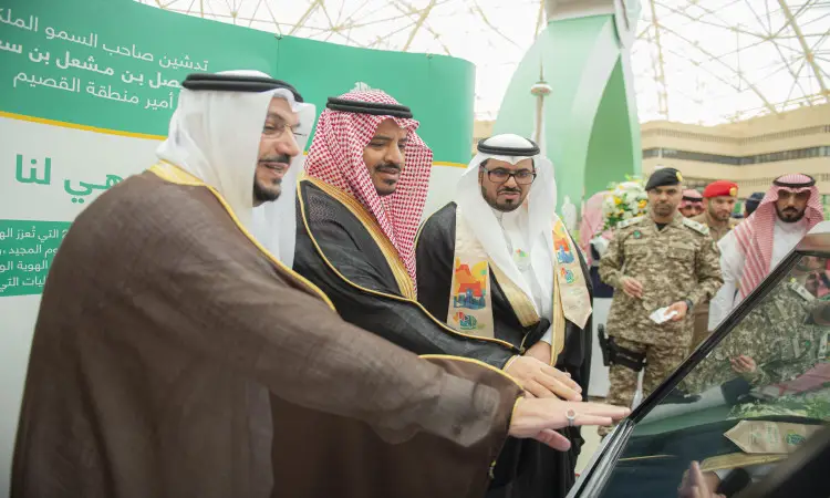 ثلاثة رجال الزي السعودي الرسمي، مشاهير ذلك الغترة السعودية أو الشماغ مع العقال والبشت السعودي، يتقدمون بهم صاحب السمو أمير منطقة القصيم، يبتسمون خلال لمسهم للشاشة خلال جامعة القصيم بمناسبة اليوم الوطني الثاني والتسعةين. ويقف بجوارهم عدد من الفريق ومنسوبي المجموعات العسكرية تحت قبة تزينها اللافتات الخضراء في الخلفية.