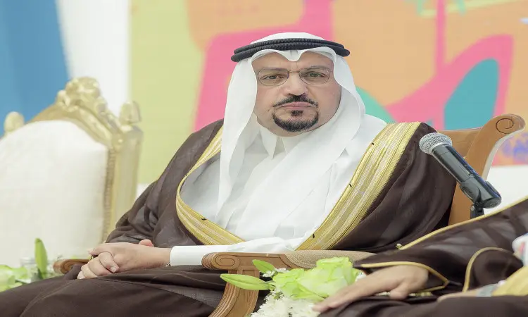 يرتدي رجل الزي السعودي التقليدي، حيث يُزين بغتة سعودية بيضاء مع عقال أسود، ويلبس بشتاً سعودياً بنياً مزخرفاً بحواف ذهبية، على كرسي فخم خلال جامعة القصيم بمناسبة اليوم الوطني الثاني والتسعين. يظهر أمامه ميكروفون مجموعة جواره من الزهور، بينما تبدو خلفية خلفية للباب.