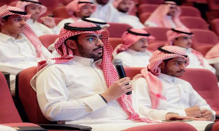 داخل قاعة في جامعة القصيم، الاتصال رجل مرتدياً الغترة والشماع والعقال والبشت السعودي، ممسكاً بالميكروفون ويلقي كلمةً، بينما يستمع الحضور باهتمام العجوز. ولذا فإن ذلك ضمن تسليط الضوء على التحول في التعليم بمناسبة اليوم العالمي للعلم.