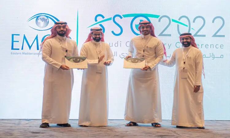 أربعة رجال على المنصة مرتدين الغترة أو الشماغ السعودي مع العقال، أخذوا البشت السعودي الرسمي. عصر كلٌ منهم شهادة ويبتسمون في المؤتمر السعودي السابع للبصريات 2022، للحفاظ على شعارات بارزة للبصريات وجامعة القصيم.