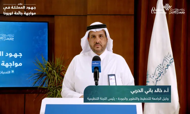 رجل ألت مرتدياً سلاحاً أبيض، غترة سعودية، عقال، وبشت سعودي عند منصة تعتمد على الميكروفونات، ملقياً كلمة حول موضوع "إدارة جيدة". ابتكاره كتب عربية وشعارات علمية المملكة العربية السعودية، في إطار يبرز جهود جامعة القصيم خلال مكافحة كورونا.