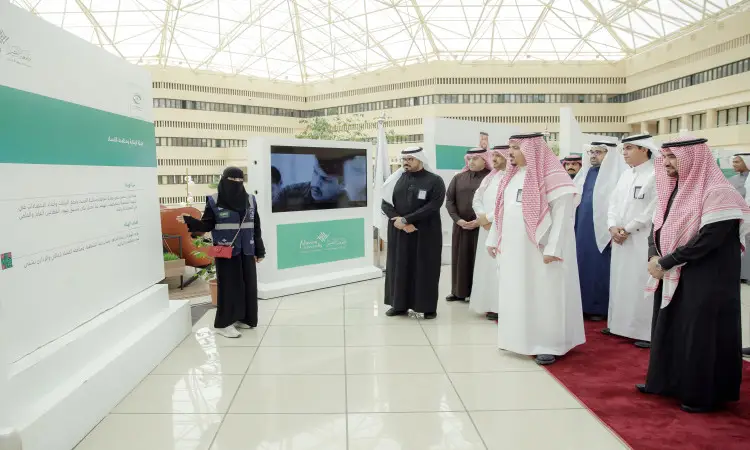 يجتمع مجموعة من الرجال وهم وهم البشت السعودي مع الشماغ والعقال في قاعة داخلية، حيث يستمعون باهتمام إلى سيدة تقدماً عرضاً توعوياً حول برنامج نزاهة، وتغطي وجهها بما في ذلك الدخل مع تعلمها المحلية. يُعرض محتوى البرنامج على لوحة تعريفية أمام الحضور، وتحديد في الخلفية شاشة كبيرة وسقف تصميمي، وذلك ضمن فعالية منظمة القصيم.