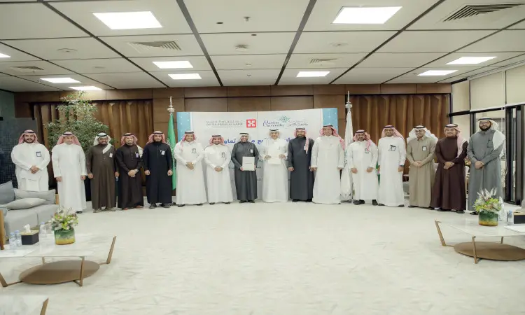 القطة مجموعة من الرجال مرتدين الغترة أو الشماغ والعقال، إضافة إلى التحالف بالشت السعودي، وآخرون ببدلات الرجال، مصطفين في صف داخل إحدى الأجنحة. يلتقط صورة الحضور أمام لوحات تحمل شعار مجموعة سليمان الحبيب الطبي، وذلك في إطار إبراز للطلاب التعاون التعاوني والشراكة التعليمية مع جامعة القصيم. مقهى في مجال طاولات الزينة بالزهور.
