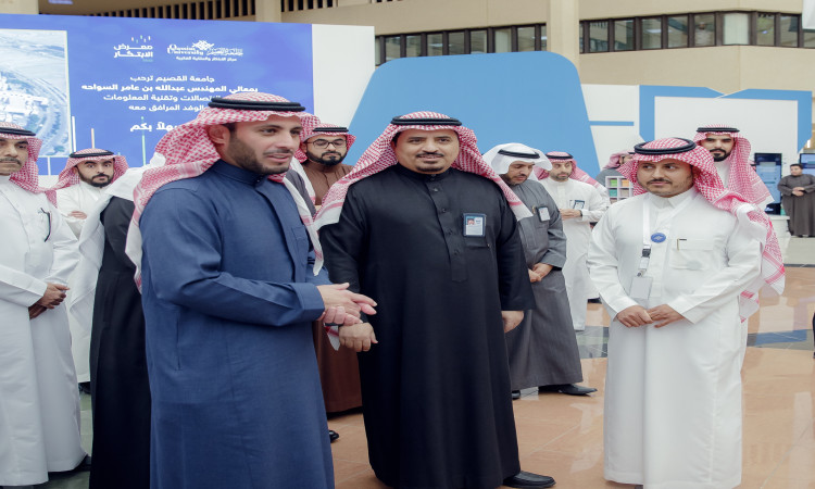 مجموعة من الرجال مرتدين الأثواب التقليدية مع الشماغ السعودي والعقال بين الفعاليات الرسمية في جامعة القصيم، حيث يرتدي البشت السعودي فوق ثيابهم. خذ خلفهم العرض ومُلصقات تعريفية باللغة العربية حول ريادة الأعمال الرقمية، كما يخرج على صدور عدد منهم بطاقات التعريف الشخصية الواضحة.