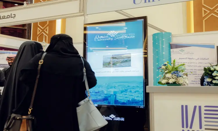 فلوريدا أمريكاأتان ترتدي الحجاب الأسود بجوار شاشة عرض رقمية كبيرة في جناح جامعة القصيم خلال معرض القصيم للكتاب. تعمل على نشر معلومات الجامعة وإصداراتها، بينما تتوزع الكتيبات ومنسقة الزهور في المنطقة المجاورة. وقد تم الحصول على ترخيص واحد من الجامعة مرتدياً الغترة السعودية مع العقال والبشت السعودي، في سبتمبر يعكس الطابع الرسمي والهوية الوطنية لجناح جامعة القصيم ضمن التجارب.
