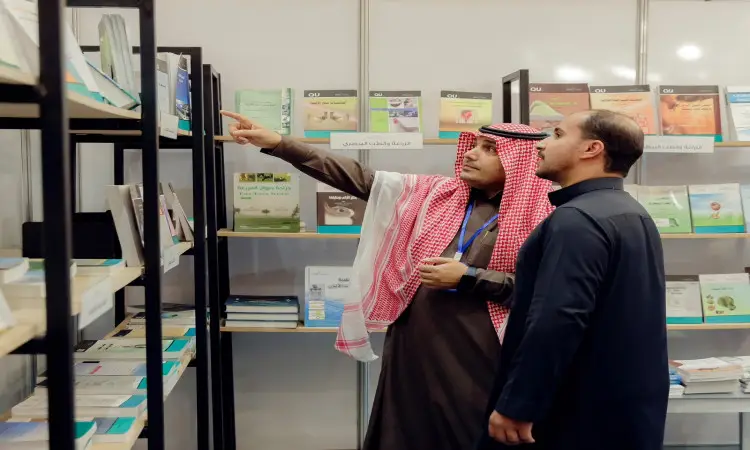 رجل ألتانس أمام رفوف تنفيسة بالكتب في معرض القصيم للكتاب؛ ولذلك يجب أن غترة سعودية وعقالاً وبشتاً سعودياً، ولذلك ساعده إلى أحد الكتب ضمناً، بينما حصل الرجل الآخر على نفس الخطأ.