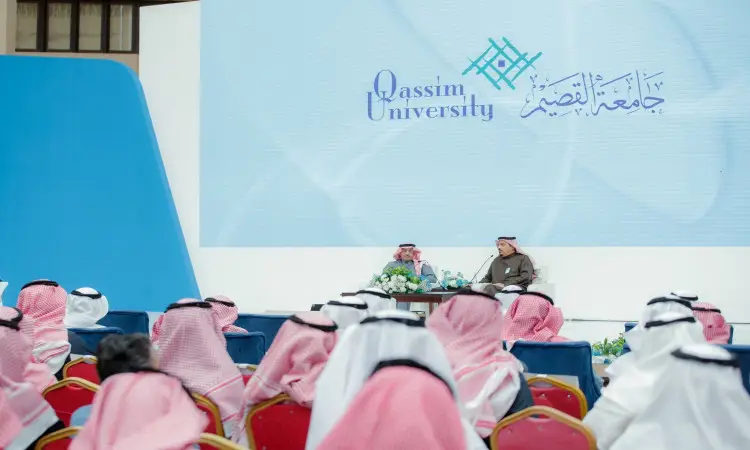 يحضرون مرتدين الغترة السعودية أو الشماغ والعقال، بالإضافة إلى البشت السعودي في قاعة الرجال، منصتين لاثنين من الاثنين على منصة مسرح جامعة القصيم، بينما تظهر شعار الجامعة بشكل ملحوظ على الشاشة الكبيرة خلفهم.