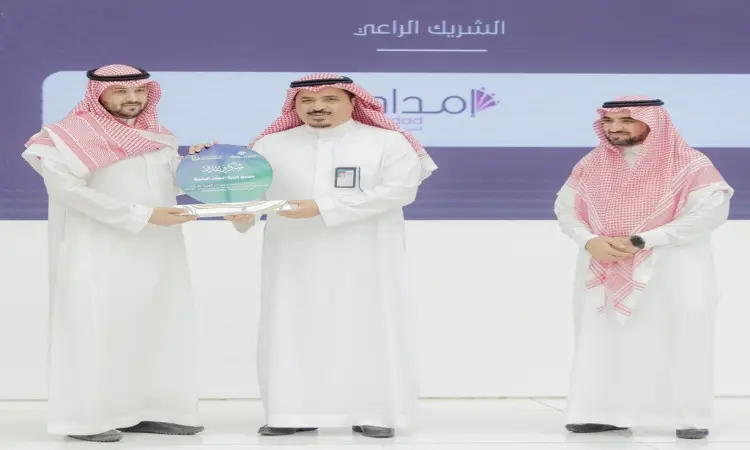 طلاء ثلاثة رجال على خشبة المسرح خلال فعاليات "يوم المهنة التقني" في القصيم، وهم تمسك الثوب السعودي الأبيض، ويضعون الغترة السعودية أو الشماغ السعودي مع العقال، فيما توشح أحدهم البشت السعودي. يتوسطهم أحد الرجال ممسكًا بدرع تكريم أزرق يقدمه له الرجل الواقف على يساره، بينما يلمس الرجل الثالث إلى جوارهم يبتسمون في مشهد يعكس روح الاحتفاء والرسمية في هذه الأكاديمية العلمية.
