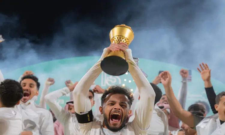 يرفع لاعب كرة القدم بفرح الكأس الذهبية فوق تسعة، محتفياً مع منتخب الجامعة الذين تألقوا بالأبيض ويضعون الشماغ السعودي والعقال، بينما يحيطون بهم في الخلفية، وذلك بعد تحقيقهم الفوز في بطولة الاتحاد الرياضي للجامعات السعودية. ويبرز اللاعب مرتدياً البشت السعودي في مشهد واضح روح الفريق والاعتزاز بهذا الإنجاز لجامعة القصيم.