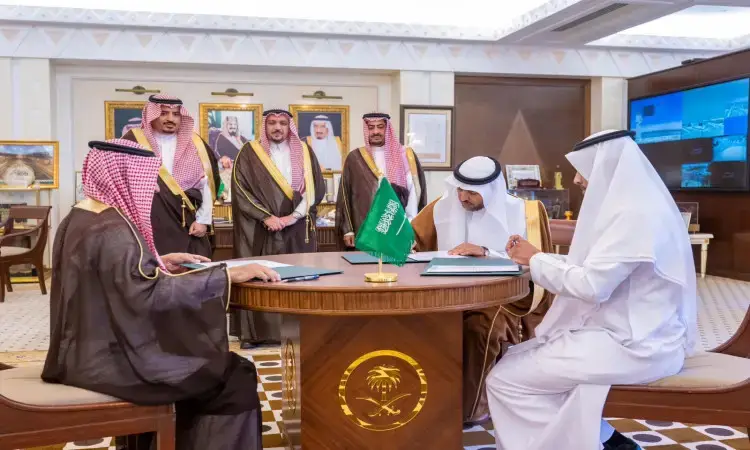 يجتمع عدد من الرجال مرتدين الغترة أو الشماغ السعودي مع العقال والبشت السعودي حول طاولة في مكتب فخم، حيث تفاعلي بتوقيع تفاهم. بارزة على علم المملكة العربية السعودية، وتبرز في خلفية صور كبار الشخصيات وأمير منطقة القصيم.