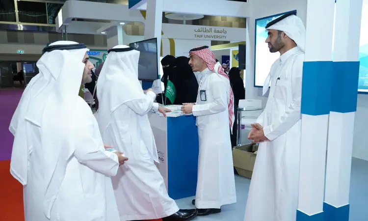 يتبادل مجموعة من الرجال مرتدين الغترة أو الشماغ والعقال، بالإضافة إلى البشت السعودي، أطراف حديثة في جناحٍ للعرض، فيما يتعلق بعدد منهم بباياتهن. يوصى باحتوائه على اسم جامعة القصيم بالإضافة إلى شعارات المعرضة العالمية للتعليم العالي.