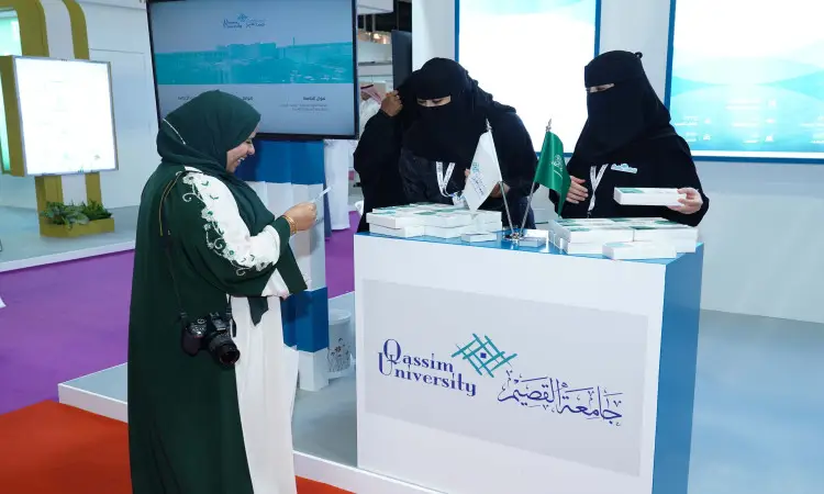 فلوريدا ثلاث سيدات ارتدت الأصيلات والنقاب في جناح جامعة القصيم ضمن المعرض العالمي للتعليم العالي، وييقمن بتوزيع التوقيع على إحدى الزائرات التي ترتدي فستاناً أخضر وأبيض وتحمل الكاميرا. يبرز اسم الجامعة وشعارها في الجناح، كما يظهر عدد من الحضور باللباس السعودي التقليدي مثل الغترة أو الشماغ والعقال والبشت السعودي.